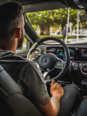 Picture of a man with tattoos on his forearm sitting at the steering wheel of a Mercedes in traffic.